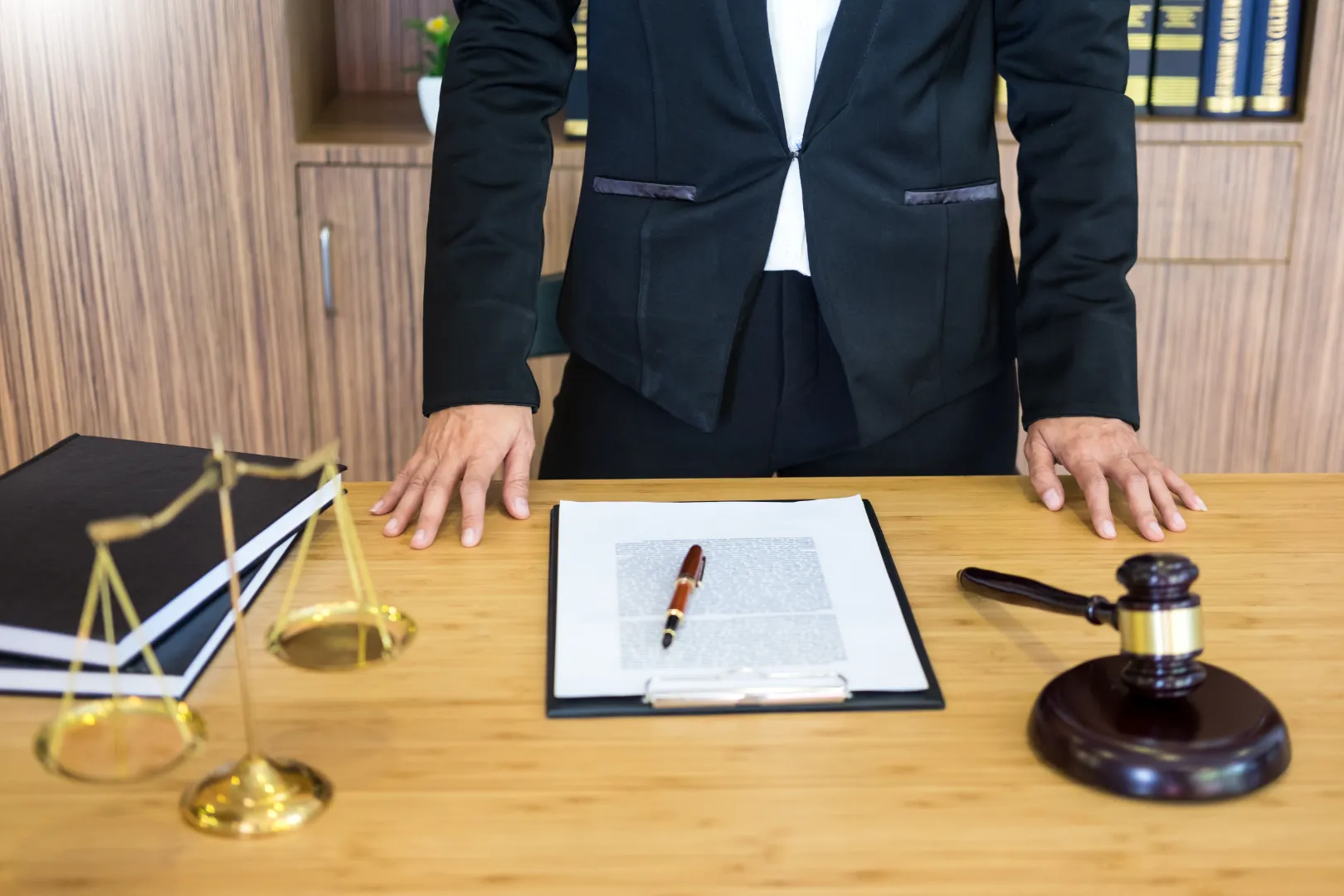 Attorney standing at a desk with a document on a clipboard, a pen, a gavel and scales of justice